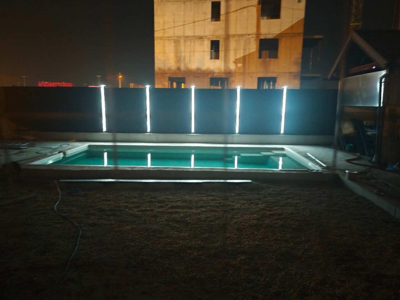 Recinzione WPC in legno composito di notte, con piscina illuminata sullo sfondo